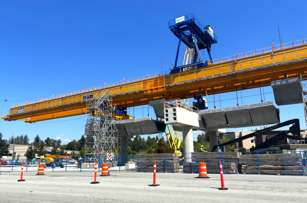 A large lifting machine called a launching gantry lifts concrete guideway segments,