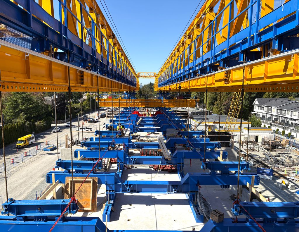 A photo taken from the top of the Surrey Sprinter launching gantry, a specialized lifting machine used to build the Surrey Langley SkyTrain elevated guideway. Blue lifting brackets are lifting elevated guideway segments into place.